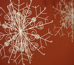 two metallic, white, glittering snowflakes hang in front of a red wall