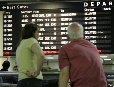 People look at an Amtrak schedule showing departure delays at Pennsylvania Station in New York.