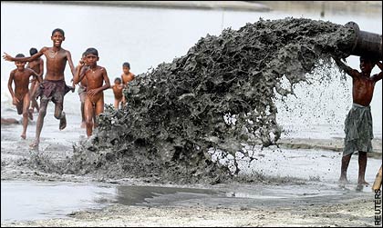 Children play near a pipe pumping mud into a low-lying area in Dhaka, Bangladesh