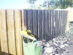 Melted recycling bin next to blackened fence